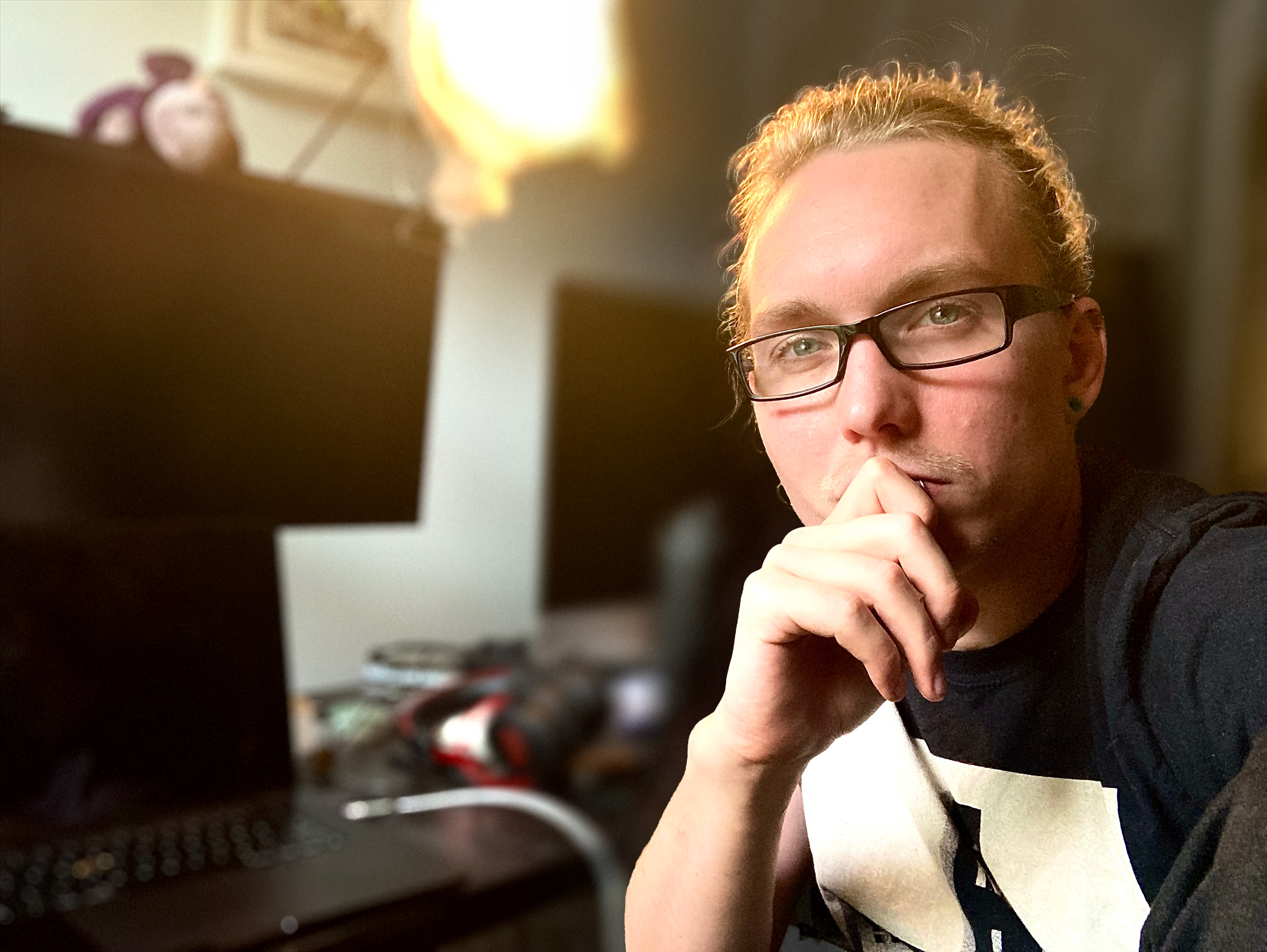 Profile Picture of iain eudailey, featuring curly blond hair and a cyan plaid flannel, his face dappled with light from the afternoon sun.